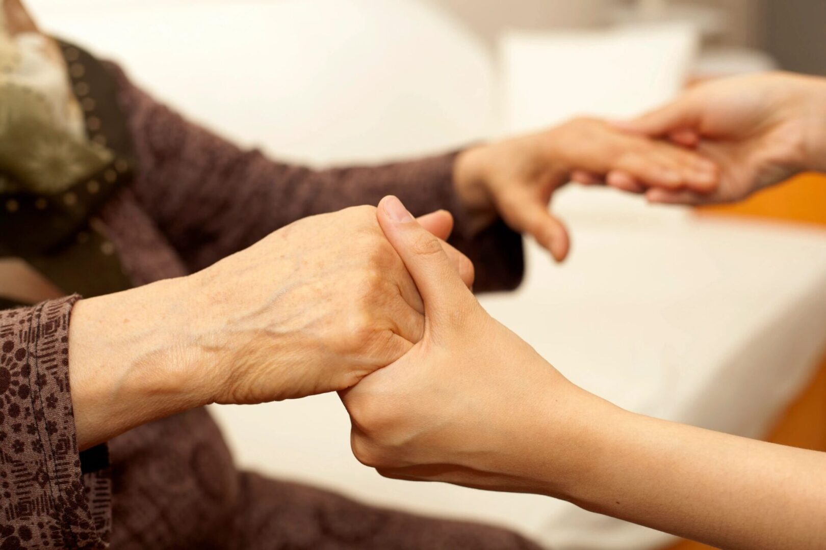 A young person holds and supports the hand of an older person, emphasizing connection and care.